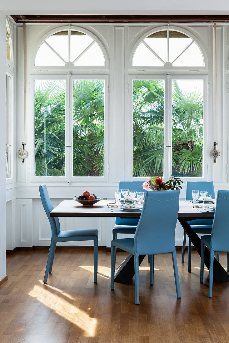 Blue chairs around dining table in window bay with arched windows
