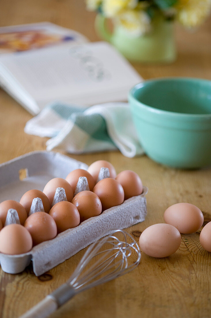 Eggs in egg carton and baking utensils on wooden table