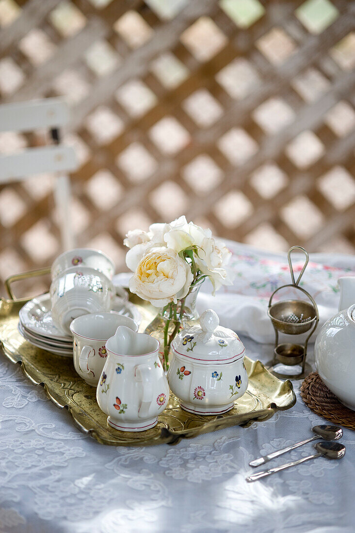 Geblümtes Kaffeeservice und Rosensträußchen auf goldenem Tablett