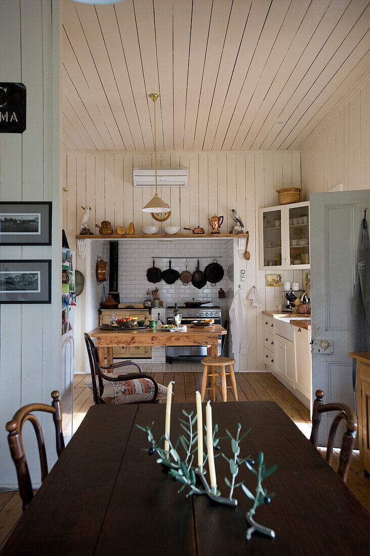 View across dining table into rustic country-house kitchen with wooden panelling