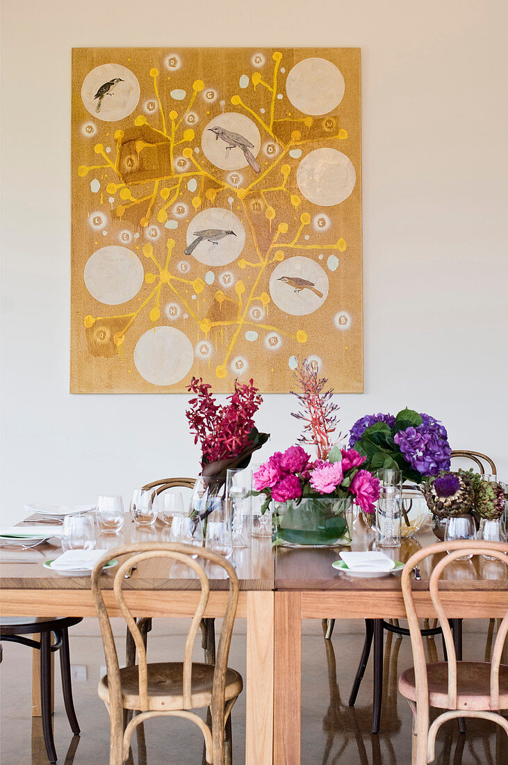 Bunte Blumensträuße auf dem gedeckten Tisch vorm Bild mit Vögeln