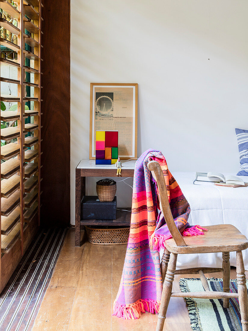 Rustikaler Holzstuhl mit bunter Decke vor Lamellenfenster