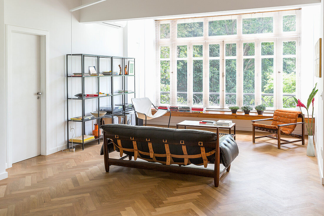 Leather sofa, chairs, shelving, and long shelf below large window in open-plan interior