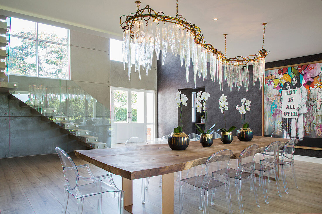 Curved chandelier with crystal icicles above table with Ghost chairs in bright, luxurious foyer