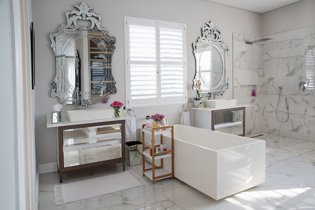 Elegant luxuriöses Bad mit weisser, rechteckiger Badewanne zwischen zwei Waschtischen mit oppulenten Wandspiegeln
