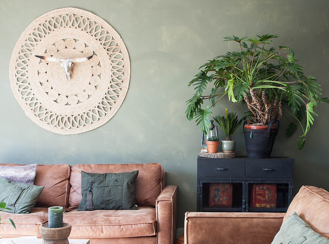 Braune Ledersofas und Wandteppich mit Tierschädel im Wohnzimmer mit grüner Wand