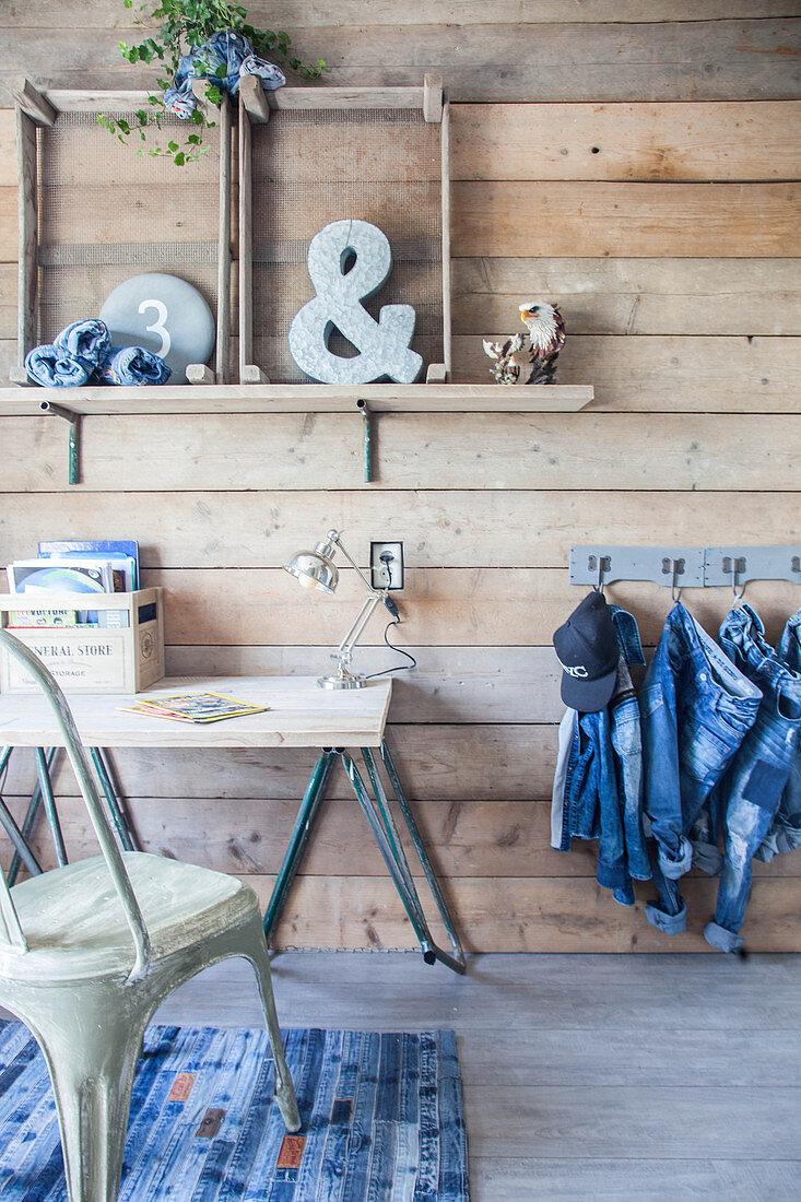 Schreibtisch an Holzwand und Kleiderstücke aus Jeans an Hakenleiste