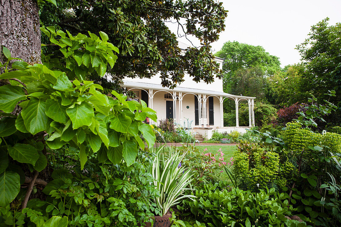 Blick durch üppiges Grün des Gartens auf ein Haus mit Veranda