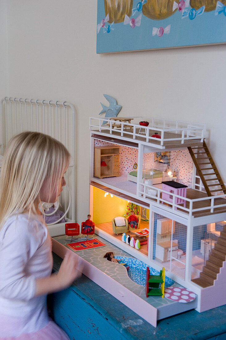 Blonde little girl playing with dolls' house with lights in interior