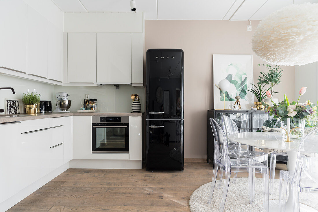 L-förmige Küchenzeile, schwarzer Kühlschrank und Essbereich mit Designerstühlen in heller Küche