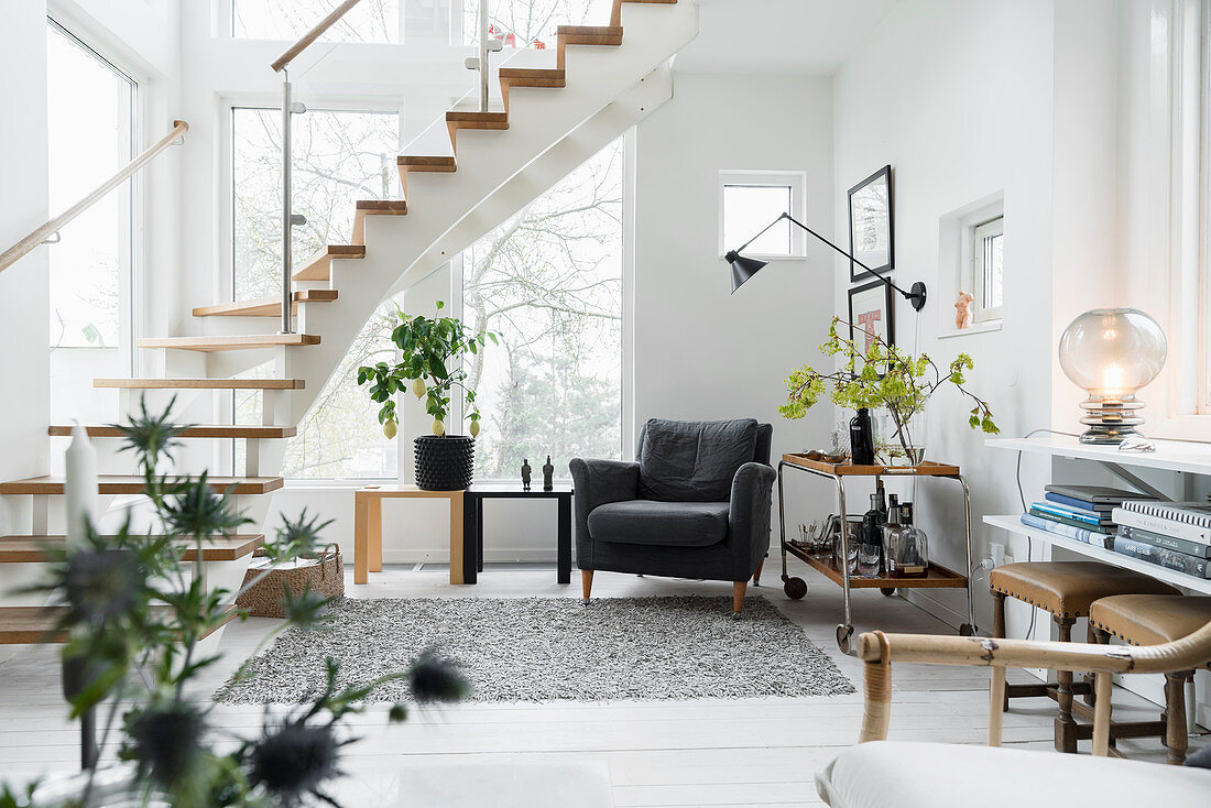 Sessel und Beistelltische vor Fenster unter Treppenaufgang in hellem Wohnzimmer