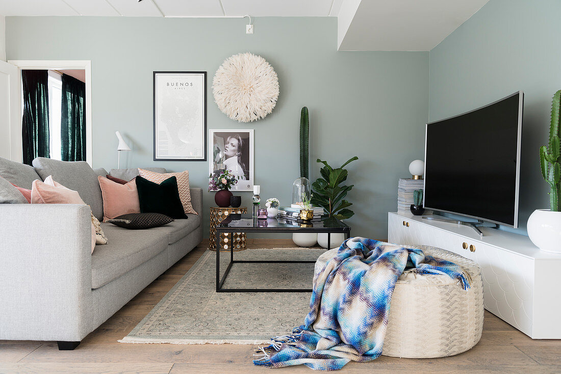 Sofa, Couchtisch, Sitzpouf, Lowboard und Fernseher im Wohnzimmer mit mintgrünen Wänden