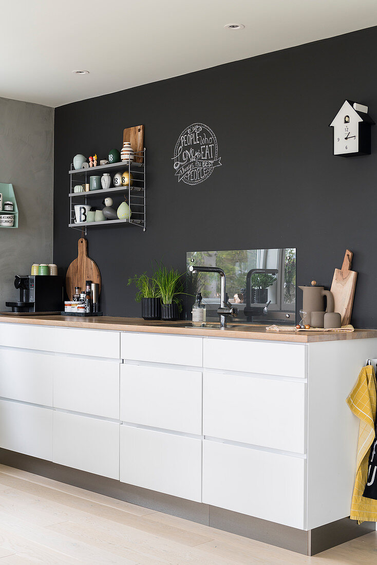 Weiße Küchenzeile mit Schubladen und Holz-Arbeitsplatte vor anthrazitfarbener Wand