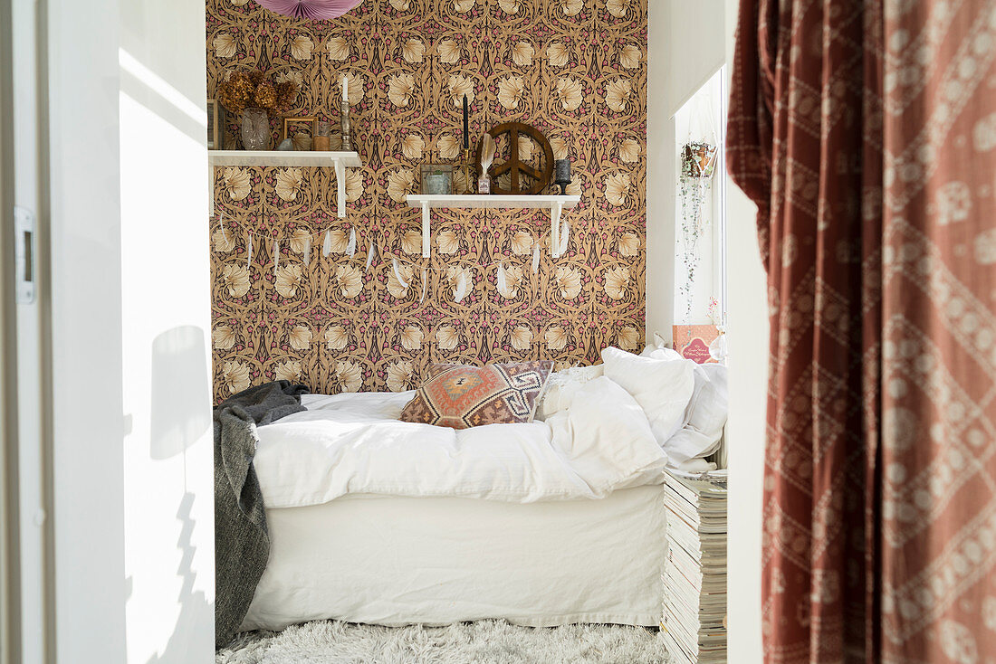 Bed with white bed linen in bedroom with wallpaper in shades of brown