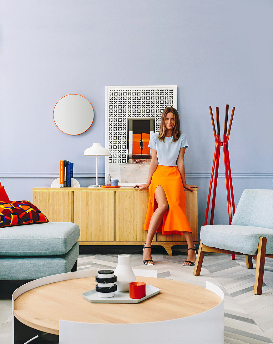 Frau lehnt am Sideboard im Wohnzimmer mit Designermöbeln