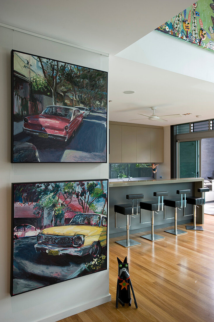 Paintings of old cars on wall of open-plan kitchen with bar stools at counter