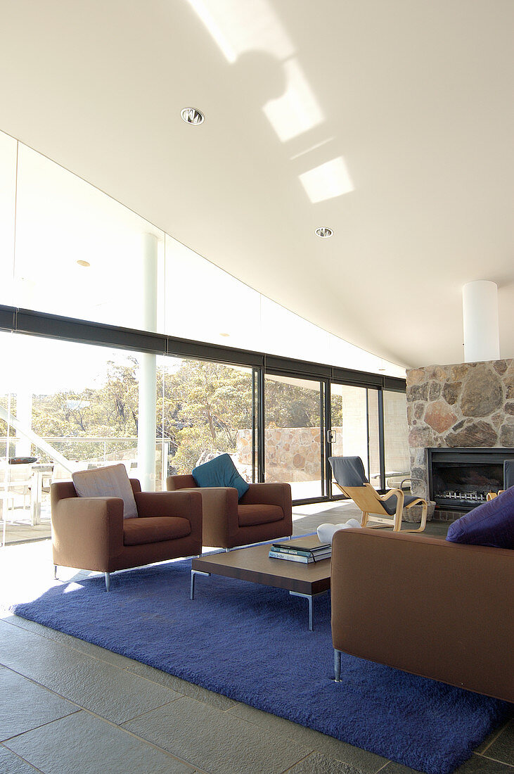 Brown sofa set, blue rug, fireplace and glass walls in lounge