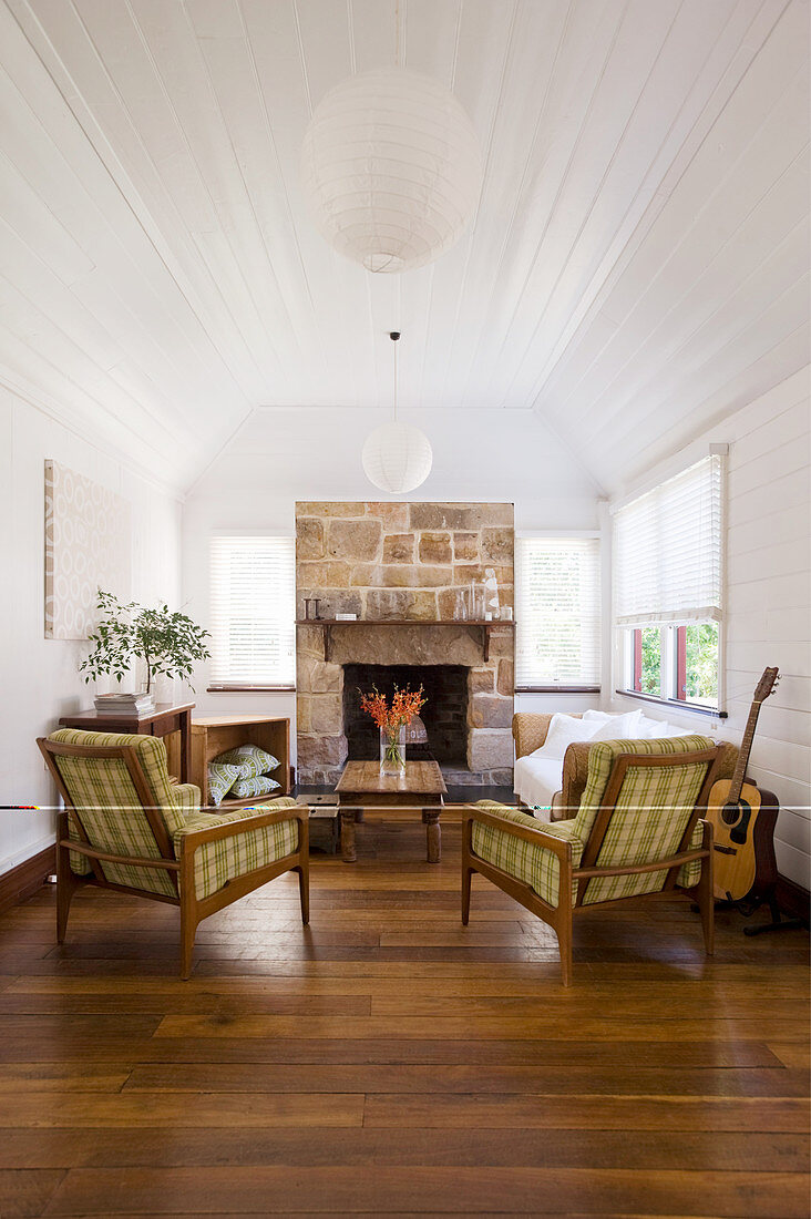 Sessel mit karierten Bezügen, Tagesbett und Couchtisch vor Kamin im Wohnzimmer mit weiß gestrichener Holzverkleidung