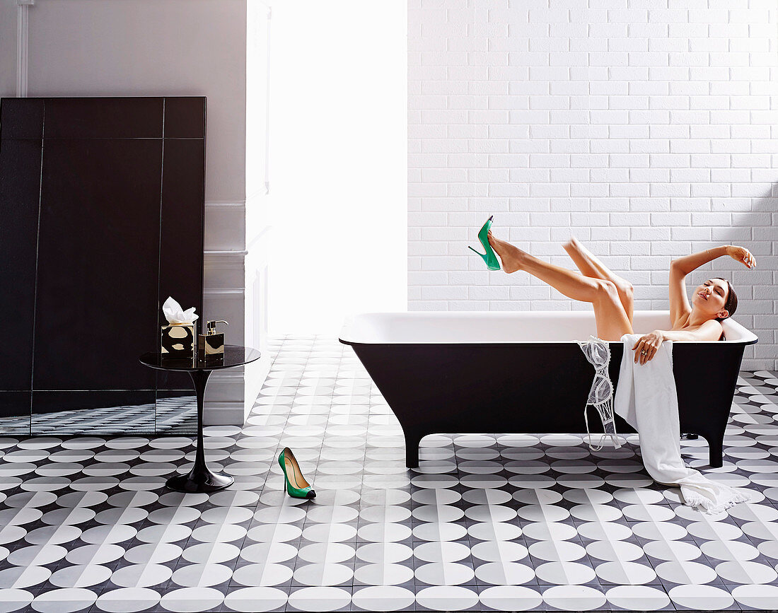 Black and white bathroom with cement tiles, woman in the bathtub