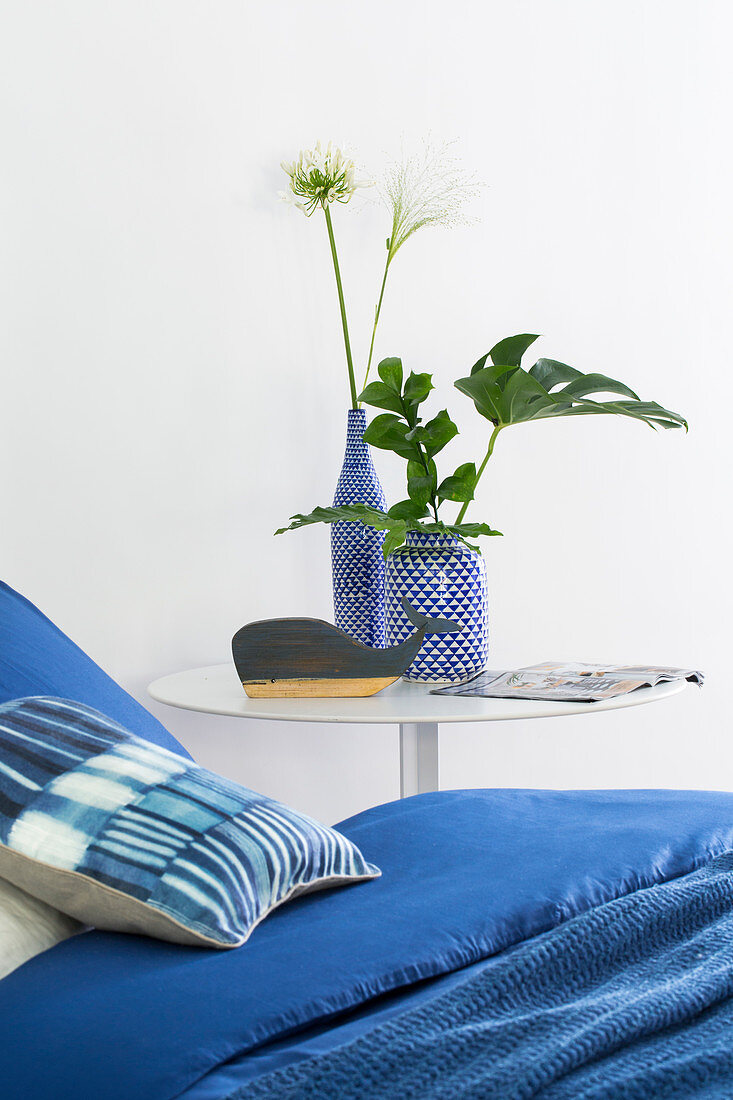 Blaue Bettwäsche auf Bett, blau-weiße Vasen mit Blätterzweig und Blume auf Nachttisch