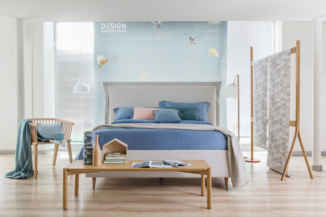Weißes Doppelbett mit Bettkopfteil und pastellblauer Bettwäsche in offenem Schlafraum mit Raumteiler