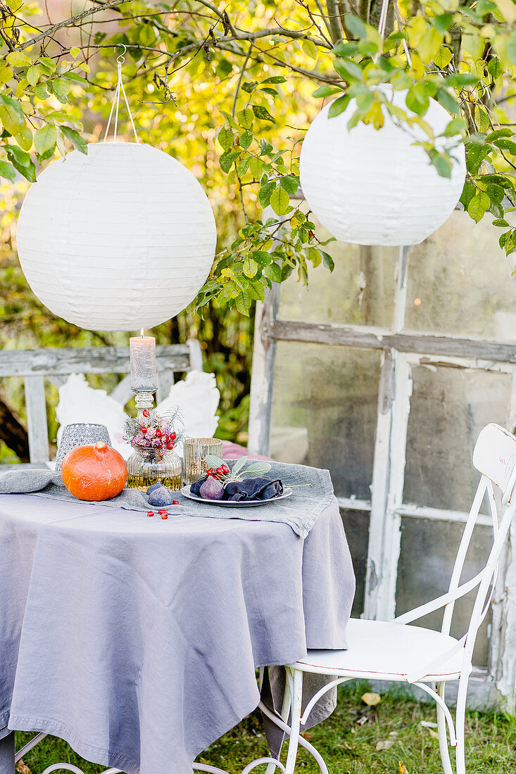 Herbstlich dekorierter Tisch unter Papierlampions im Garten