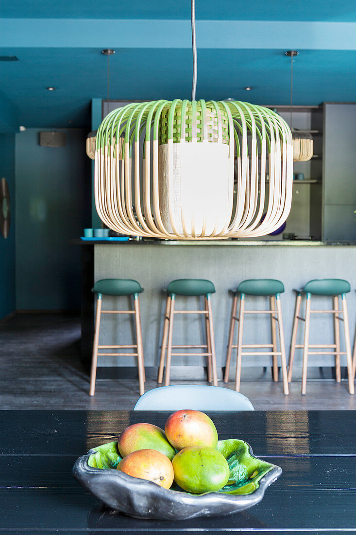 Fruit bowl below ceiling lamp and bar stools in background