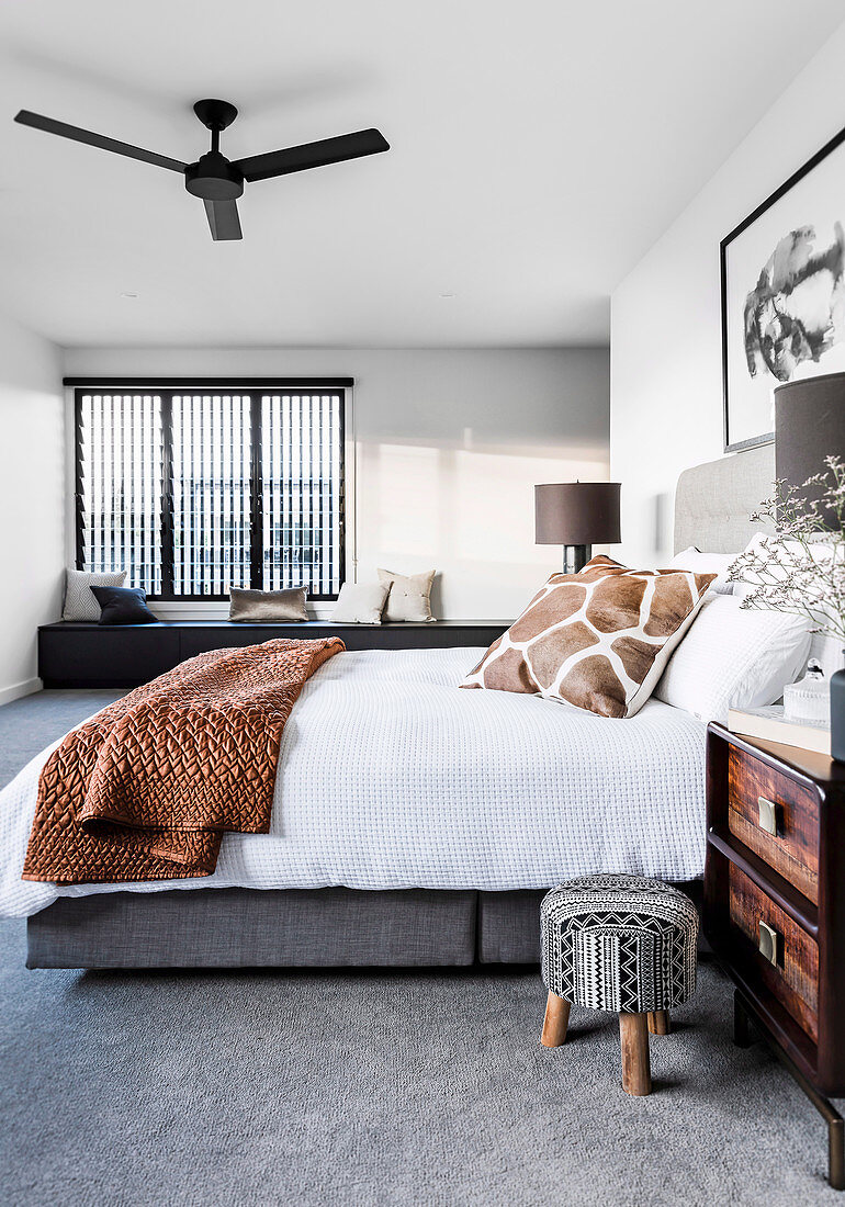 Double bed in the bedroom with gray carpeting, in the background a bench