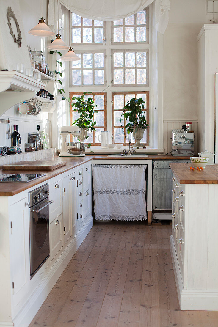 White kitchen counters with wooden worksurfaces and houseplants in front of lattice window
