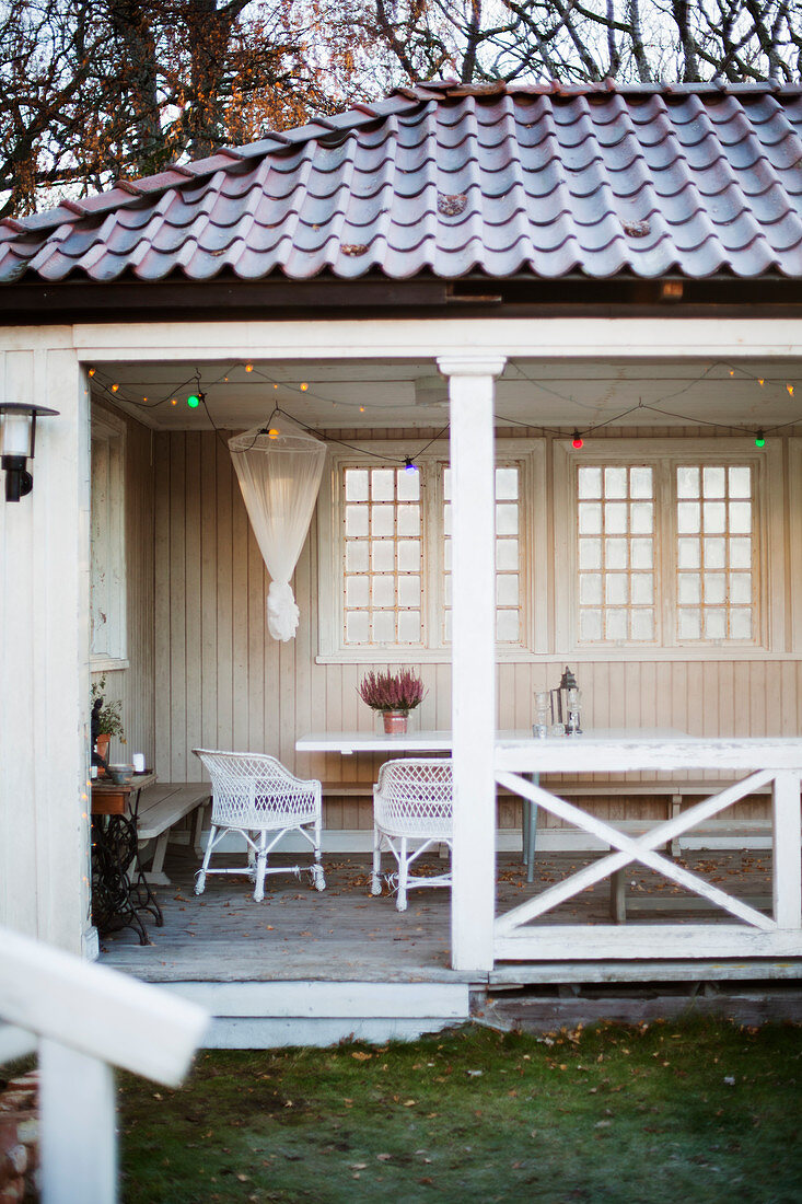 Table, rattan armchair and fairy lights in summerhouse with lattice windows
