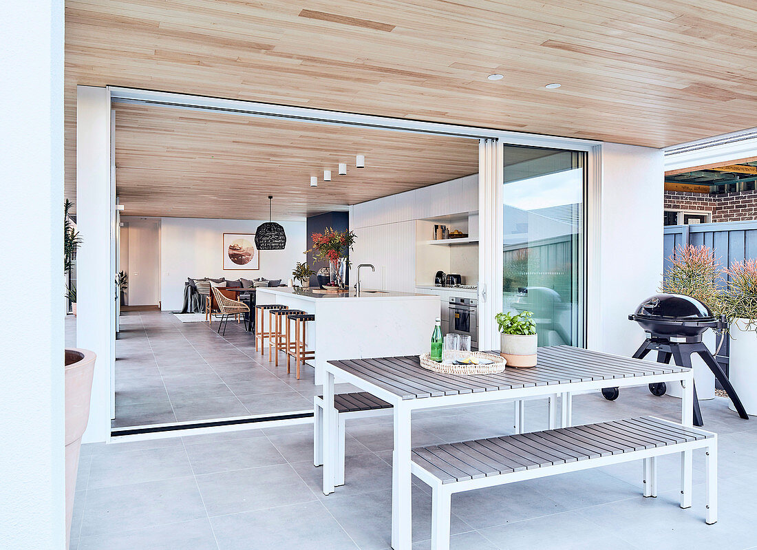 Modern dining area on covered terrace, view into open living room