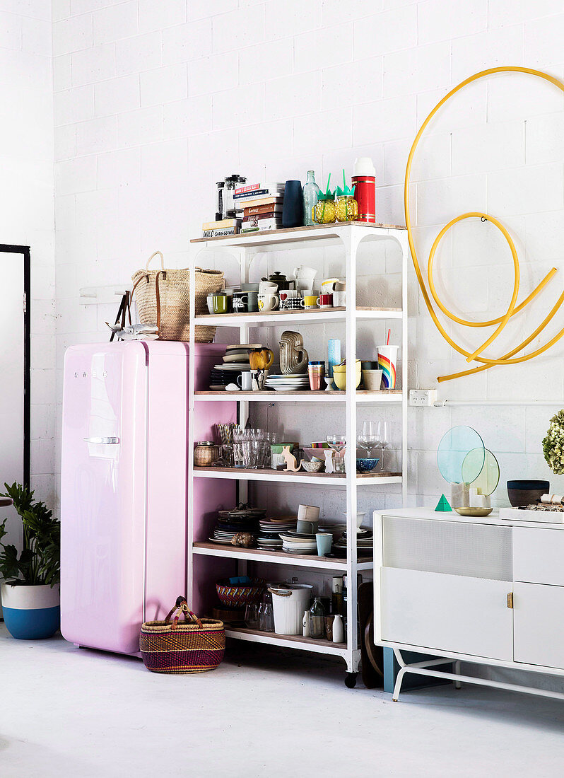 Offenes Regal mit Geschirr neben rosa Kühlschrank, gelbes Schlauch als Wanddekoration