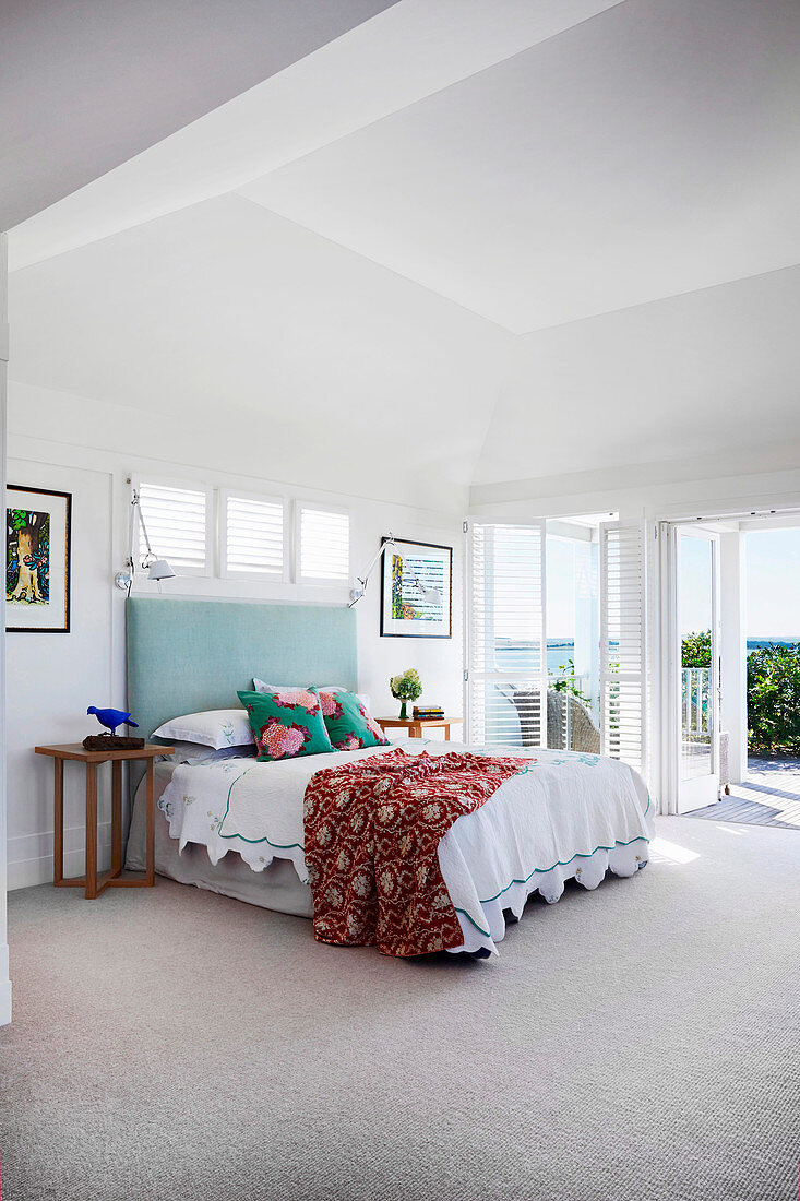 Double bed with a high mint green headboard in a light-flooded beach house