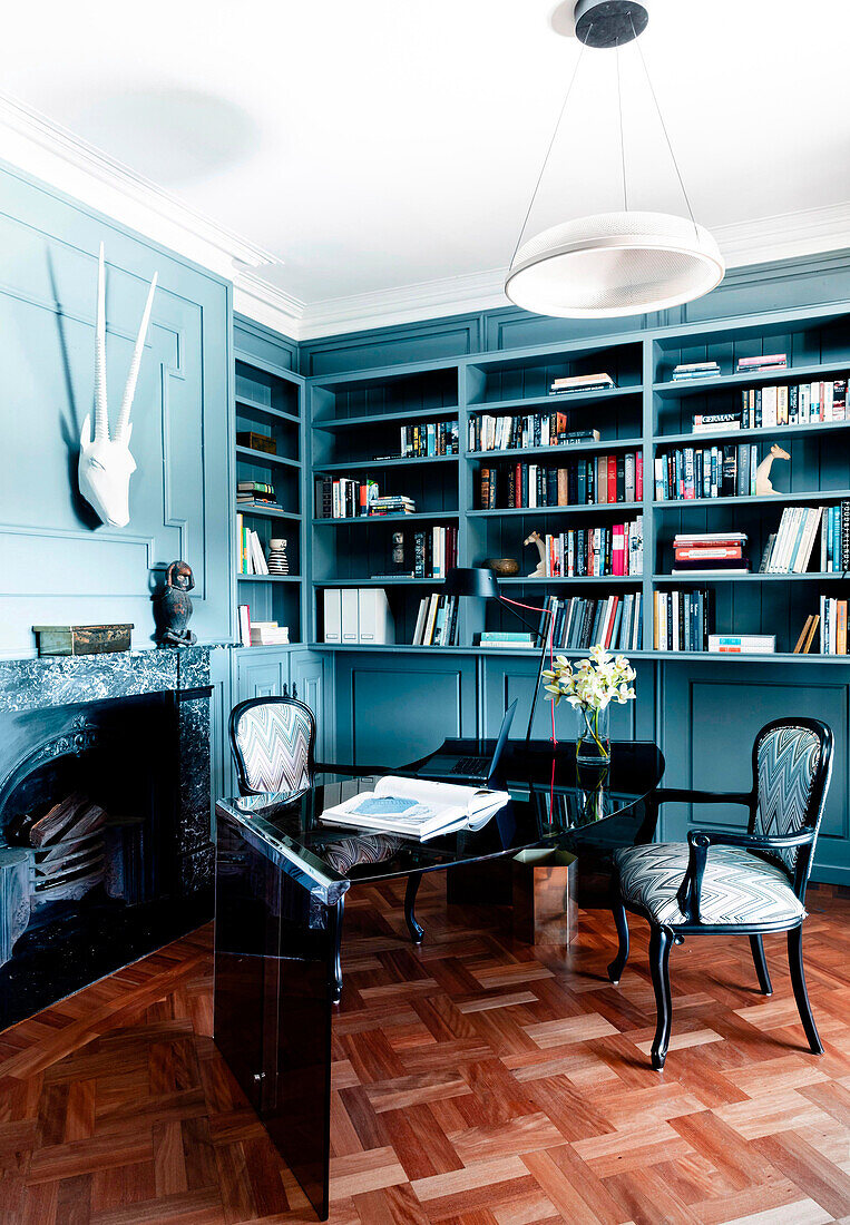 Baroque chairs on modern desk in front of shelves and fireplace