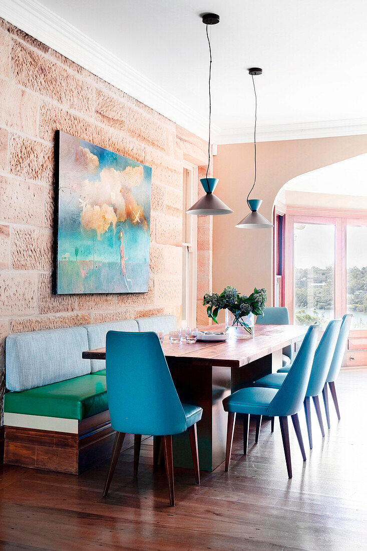 Dining table with bench and blue upholstered chairs in front of a natural stone wall