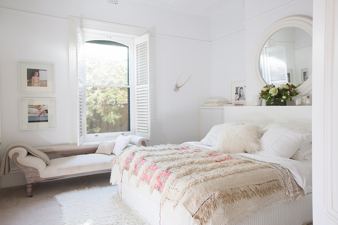 Doppelbett mit Tagesdecke und Chaiselongue vor Fenster in weißem Schlafzimmer