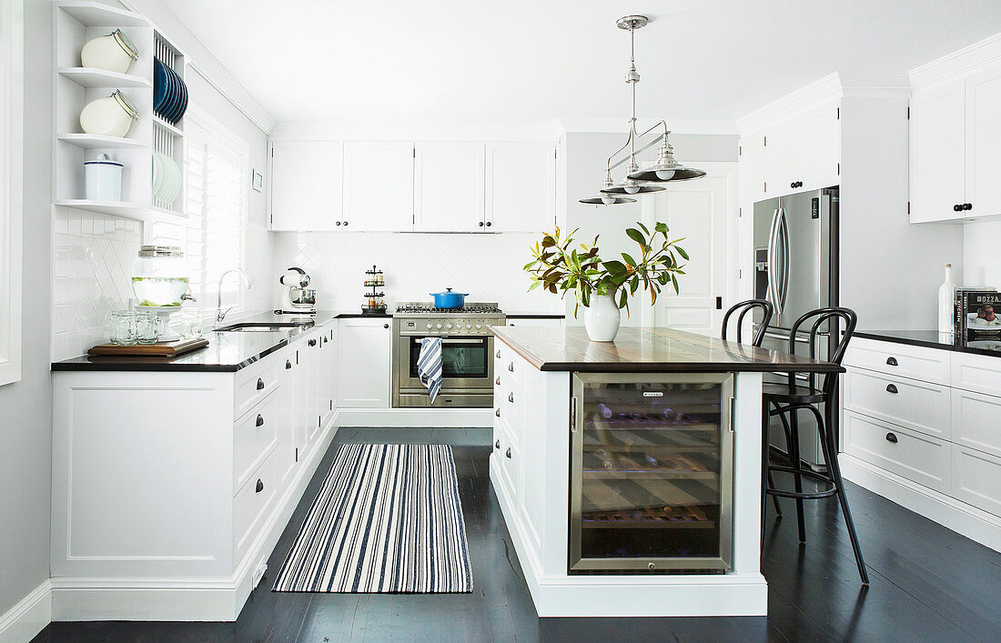 Kücheninsel mit Weinkühler und Barhocker in weißer Küche dunkler Fußboden