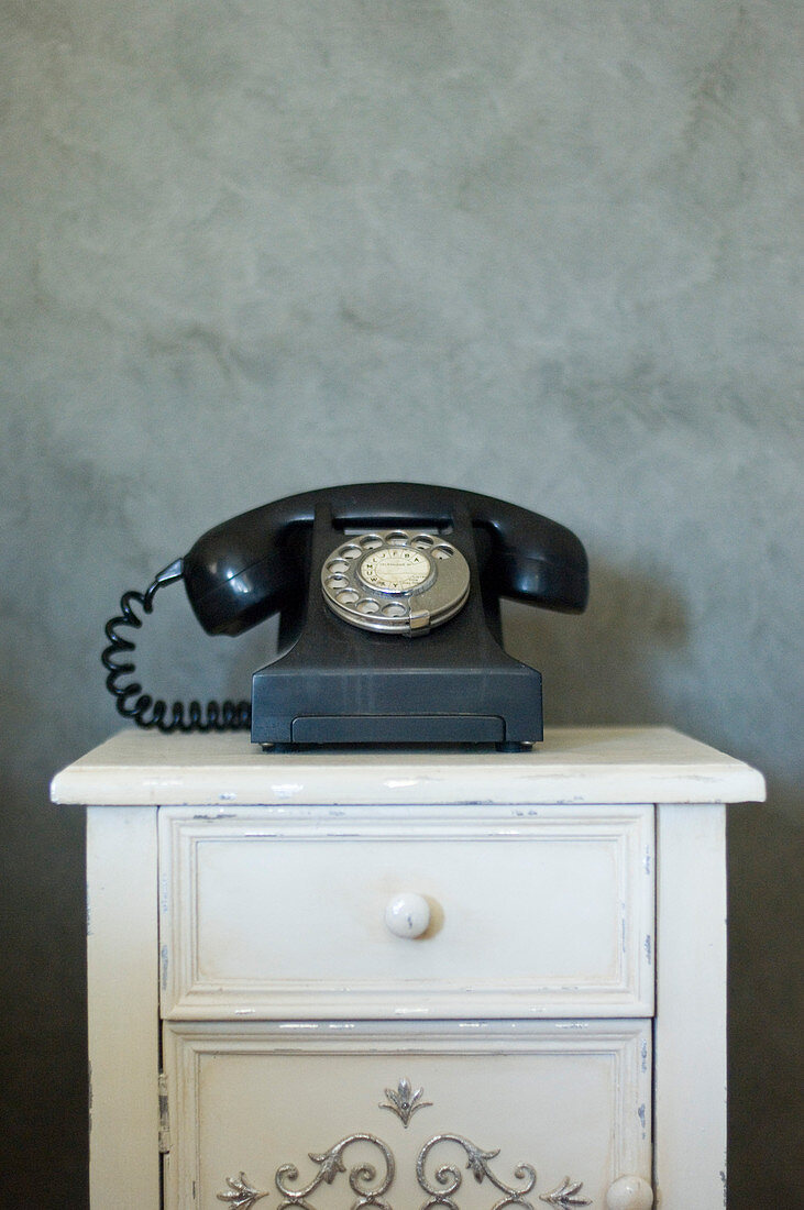 Old telephone on cabinet against mottled grey wall
