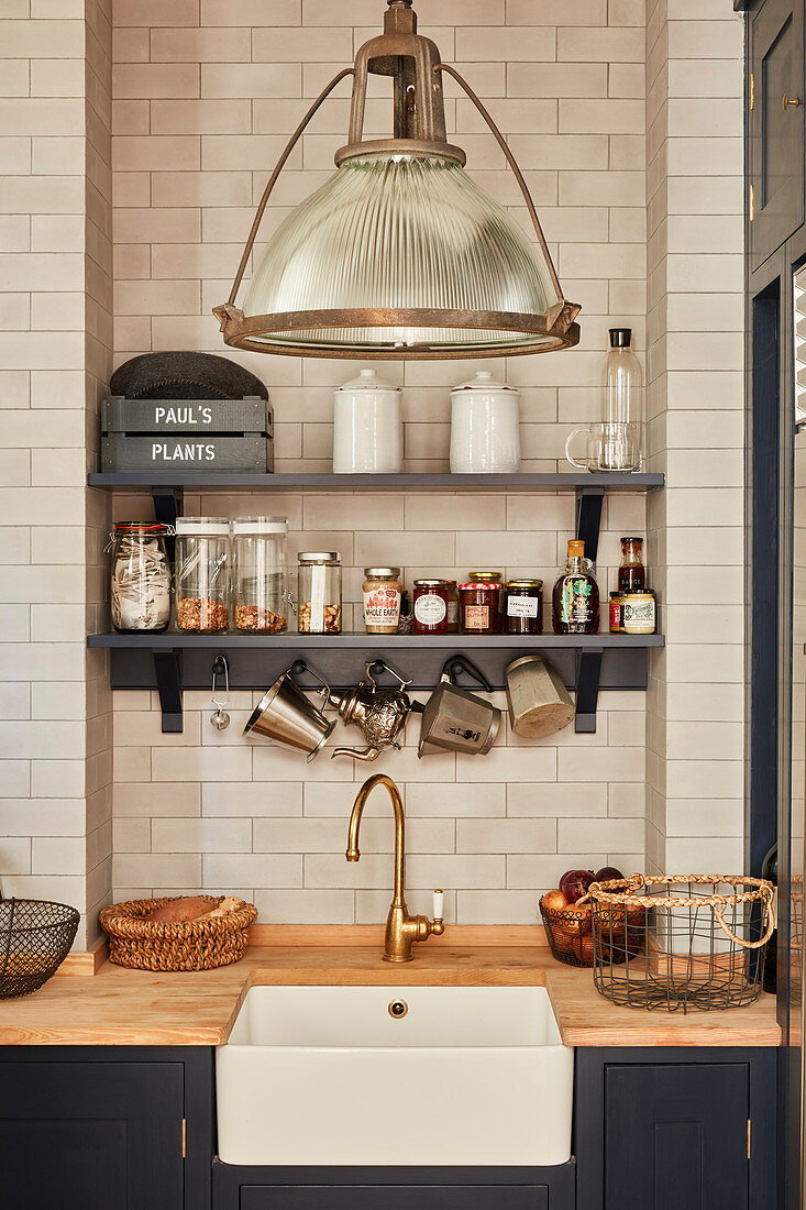 Regal mit Vorratsgläsern an gefliester Wand, darunter Küchenzeile mit integriertem Spülbecken und Holzarbeitsplatte