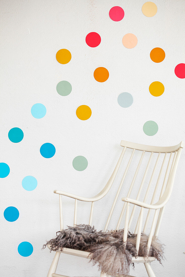 Fur rug on chair below multicoloured polka dots on wall