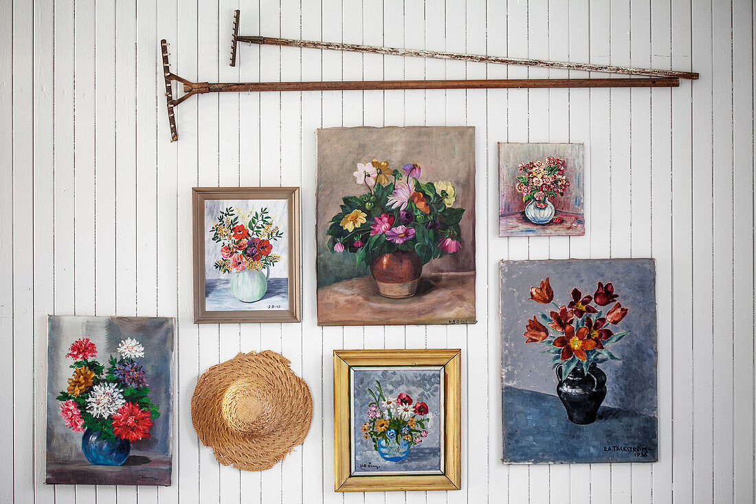 Floral pictures, vintage rakes and hat on white-painted wooden wall