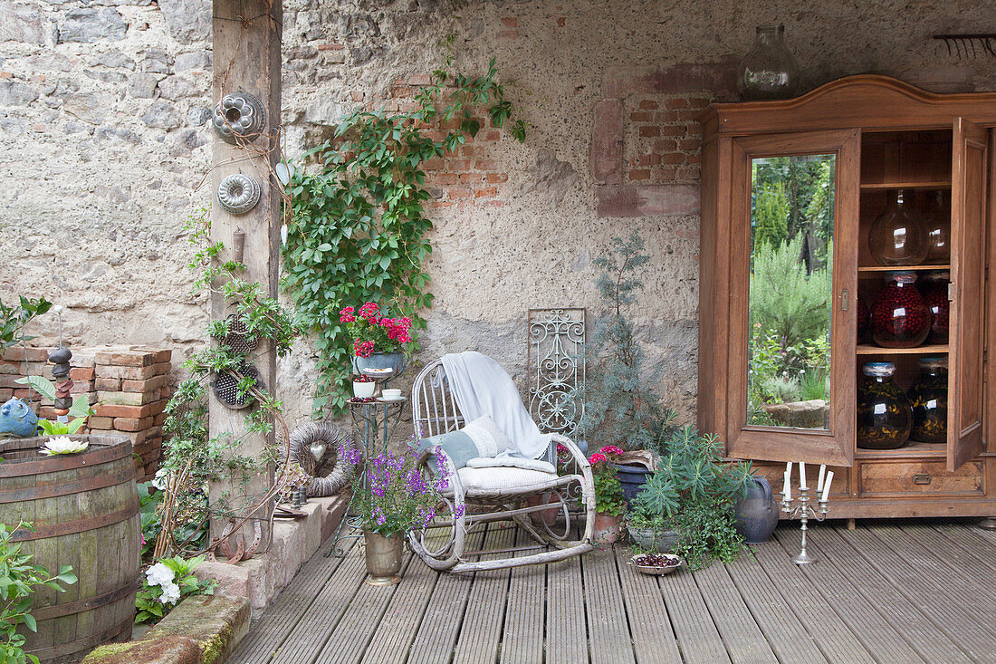 Holzschrank mit großen Einmachgläsern und Schaukelstuhl auf überdachter Terrasse