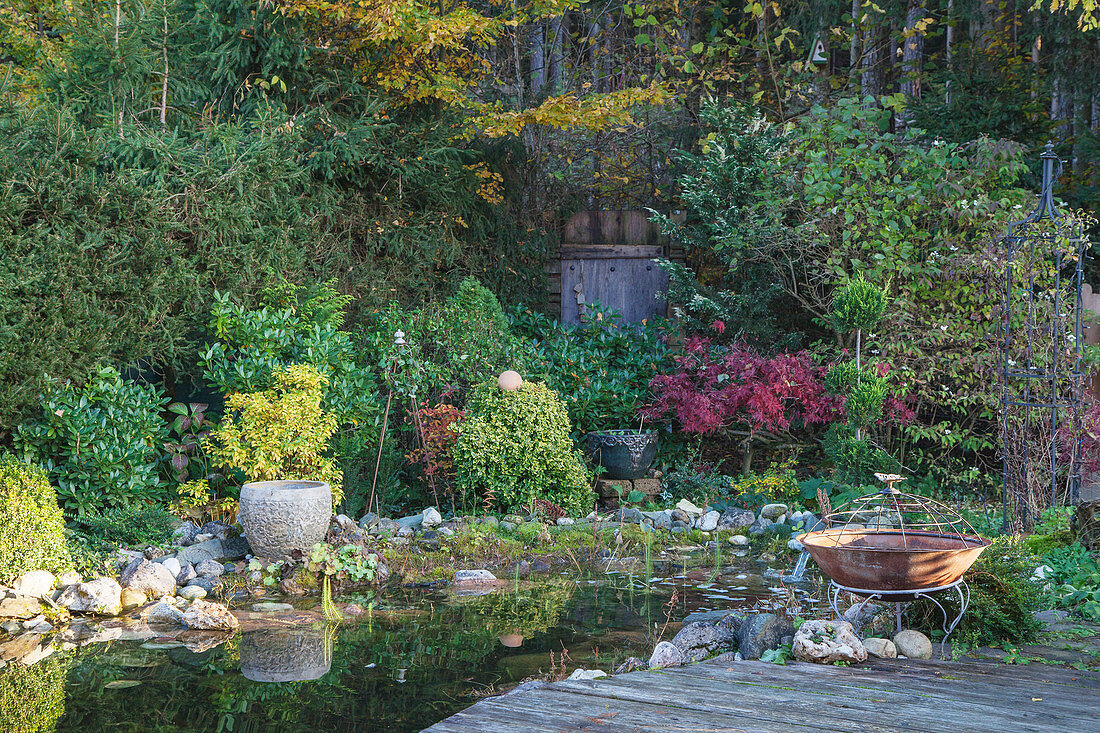 Pond in mature garden with fire bowl in foreground