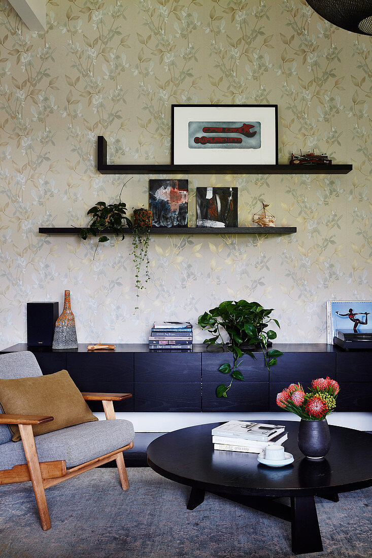 Retro armchair and black furniture in front of floral wallpaper in living room