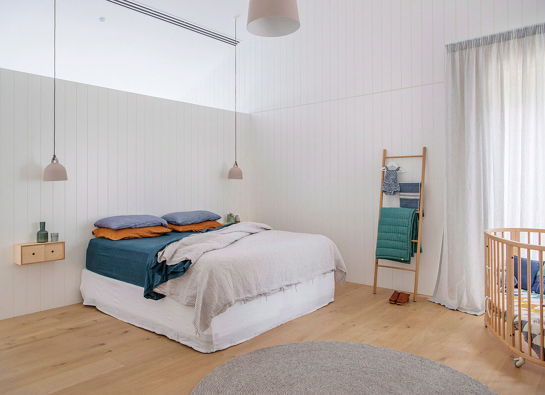Bed under skylight in simple bedroom with cot