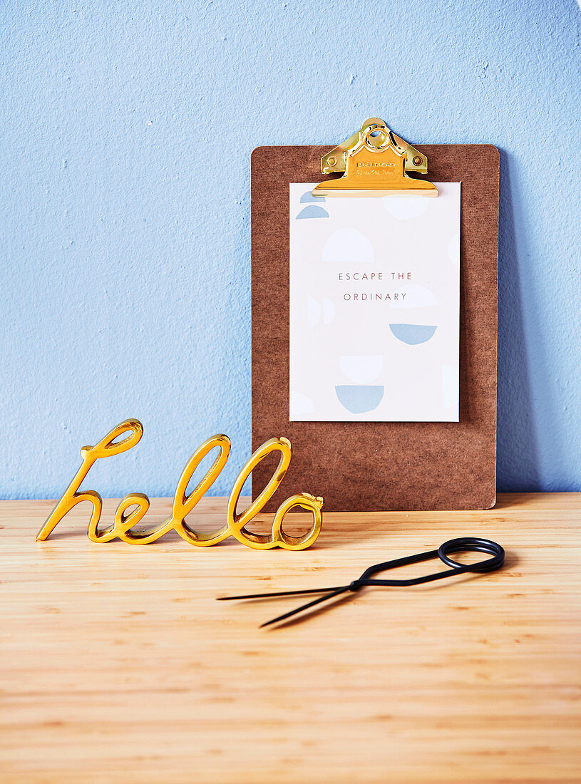 Golden decorative writing and clipboard with a saying on a light blue wall