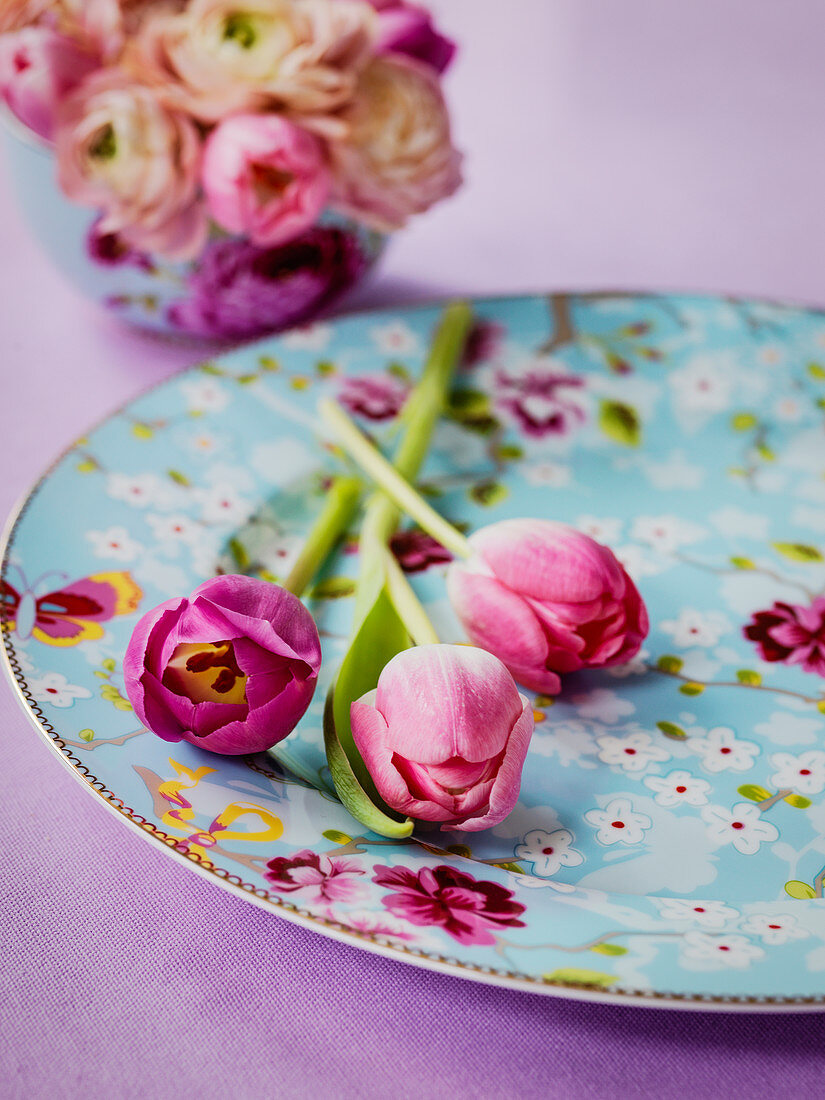 Pinkfarbene Tulpen auf hellblauem Teller mit Blütenmotiven