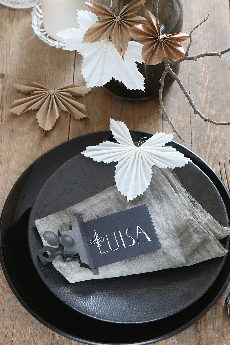 Namensschild auf schwarzem Teller und Blätter aus gefaltetem Papier