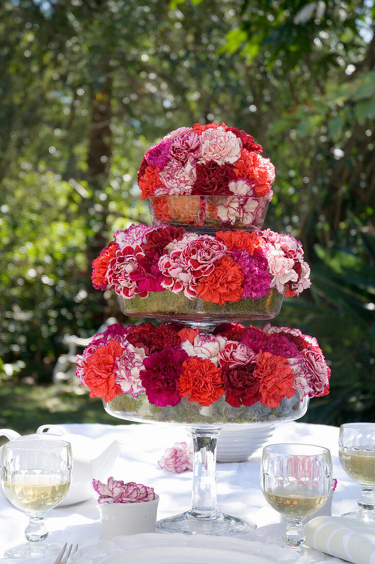 Carnations in shades of red arranged on cake stand on set table in garden