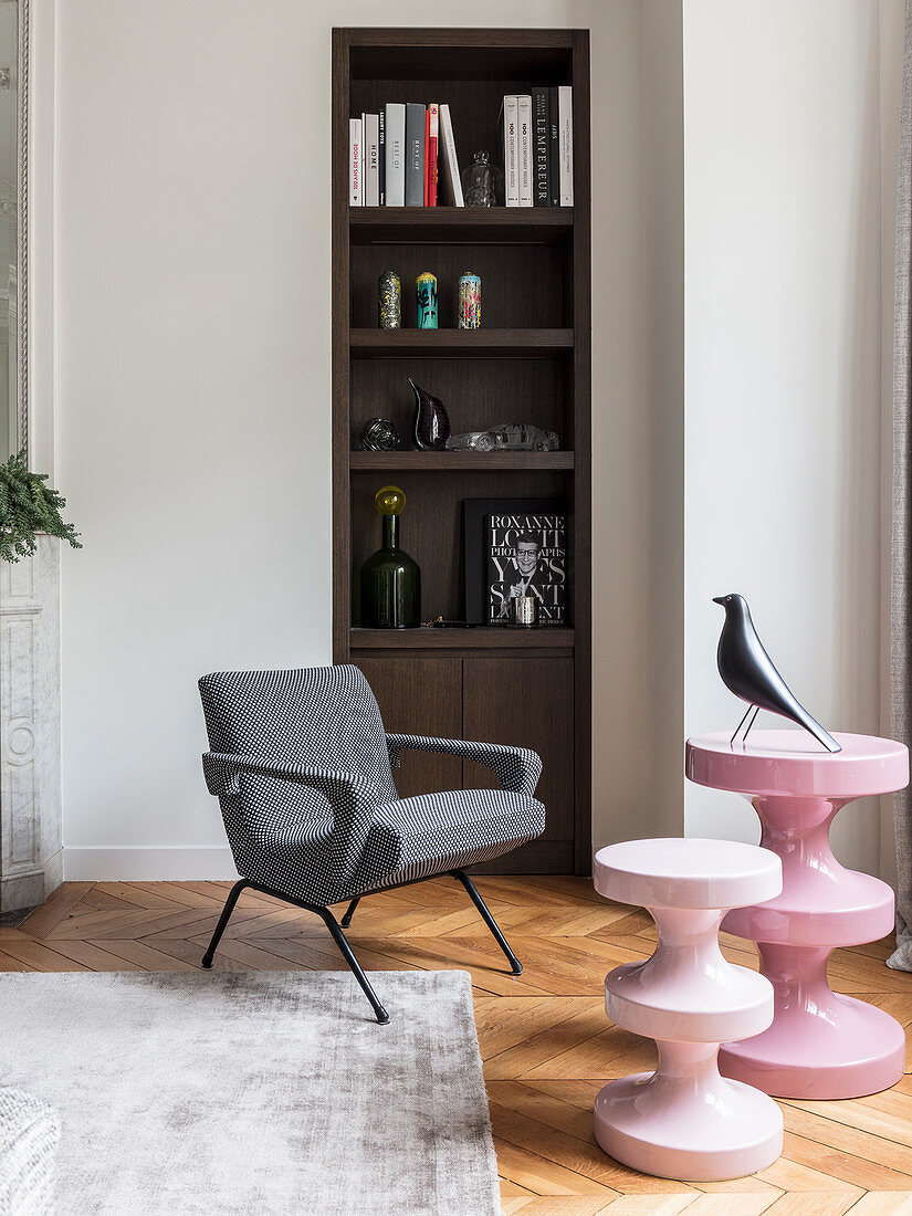 Pink, modern side tables and armchair in front of shelves